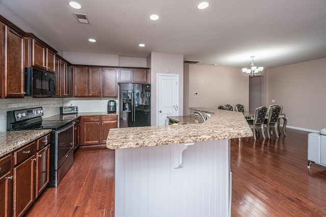 kitchen featuring a breakfast bar area, backsplash, dark hardwood / wood-style flooring, black appliances, and a center island with sink