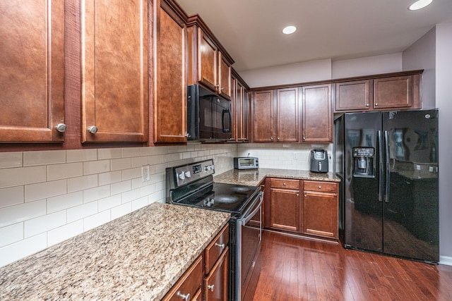 kitchen with light stone countertops, dark hardwood / wood-style floors, backsplash, and black appliances