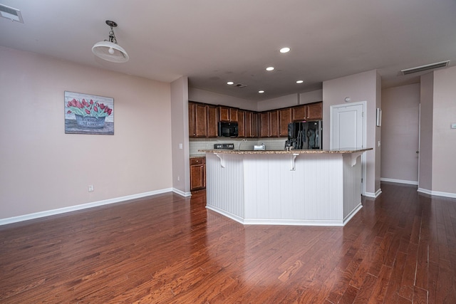 kitchen with dark wood-type flooring, a breakfast bar area, black appliances, a center island with sink, and decorative light fixtures