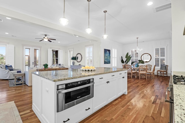 kitchen with light stone countertops, ceiling fan with notable chandelier, decorative light fixtures, white cabinets, and hardwood / wood-style floors