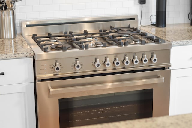 details featuring white cabinetry, decorative backsplash, stainless steel gas stove, and light stone countertops