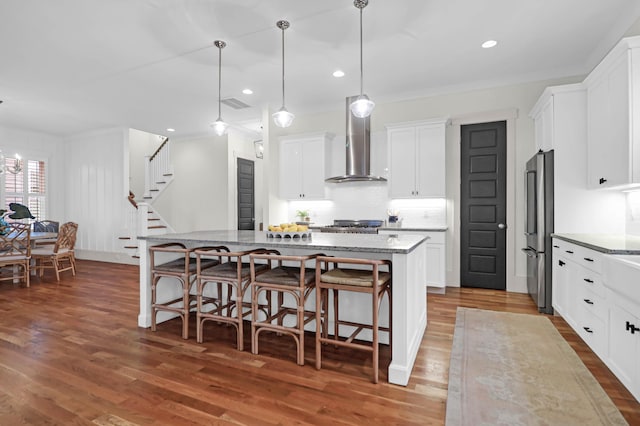 kitchen featuring a center island, wall chimney range hood, high end refrigerator, a breakfast bar, and white cabinets