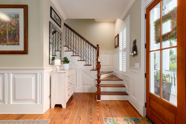 foyer entrance featuring a decorative wall, light wood-type flooring, crown molding, a wainscoted wall, and stairs