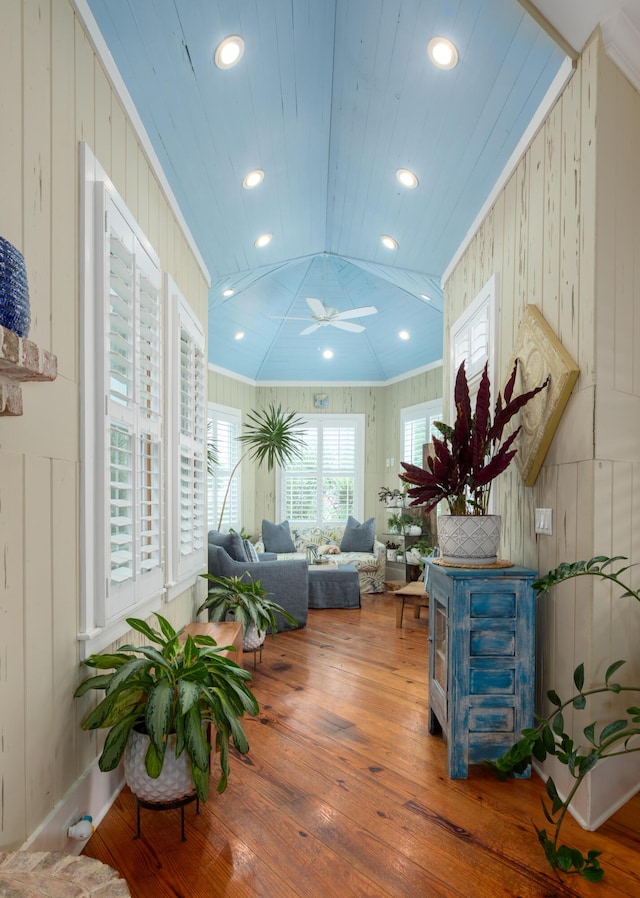 living area featuring hardwood / wood-style flooring, a ceiling fan, wooden walls, recessed lighting, and ornamental molding