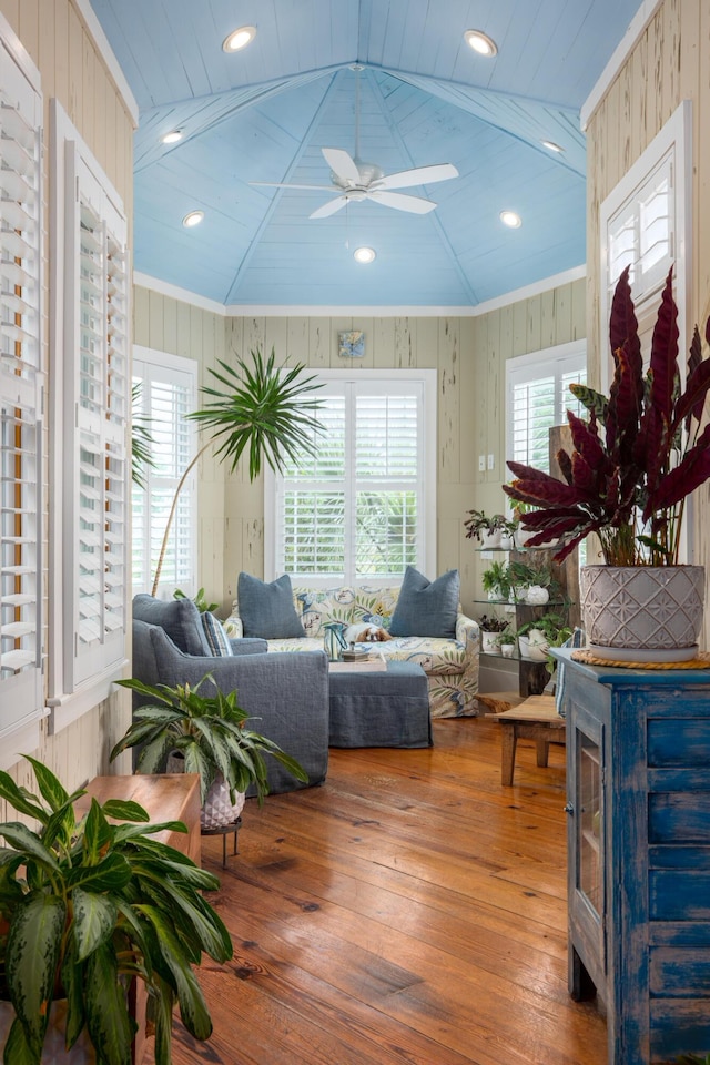 living area with wood-type flooring, ceiling fan, ornamental molding, and wooden walls