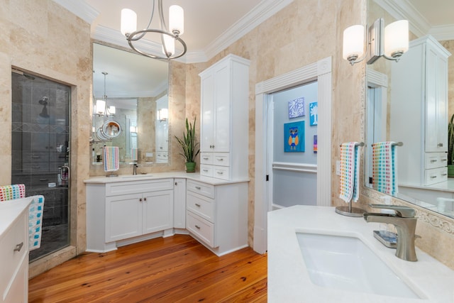 bathroom with ornamental molding, a chandelier, wood finished floors, a shower stall, and two vanities