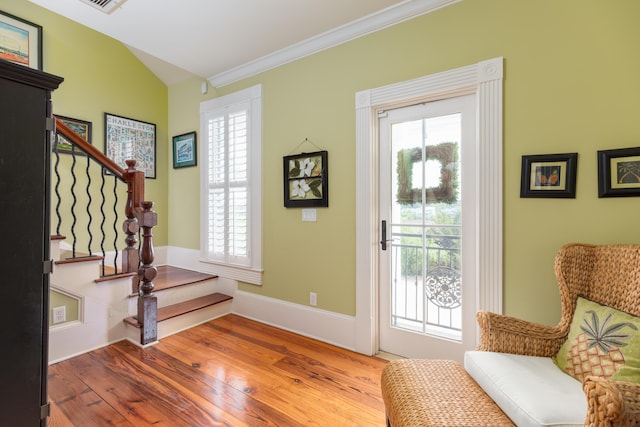 foyer featuring healthy amount of natural light, wood finished floors, stairway, vaulted ceiling, and ornamental molding
