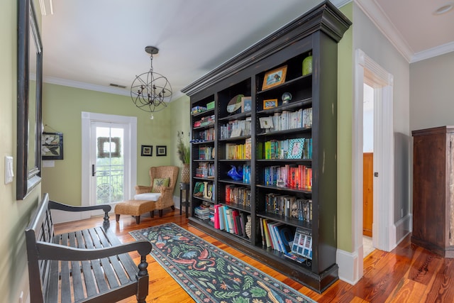 living area with a chandelier, crown molding, wood finished floors, and baseboards