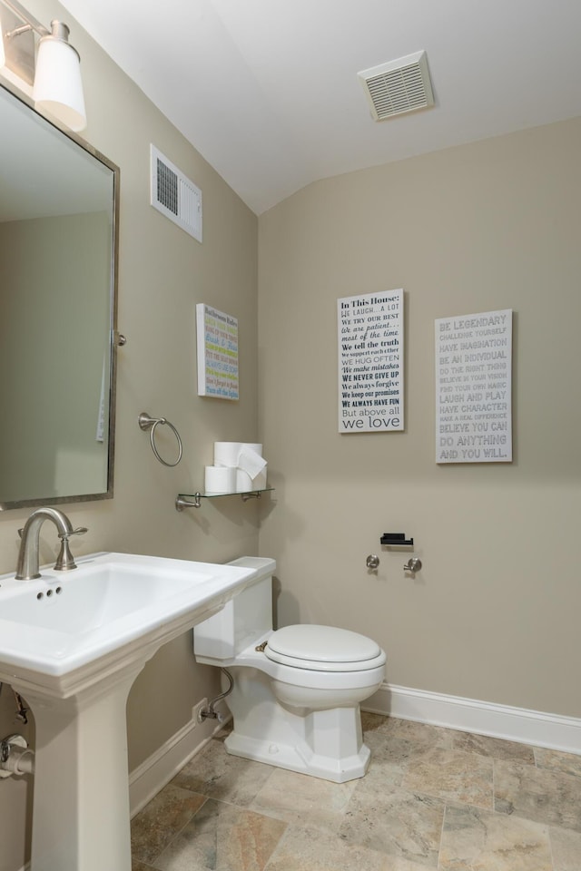 bathroom with toilet, baseboards, lofted ceiling, and stone finish floors