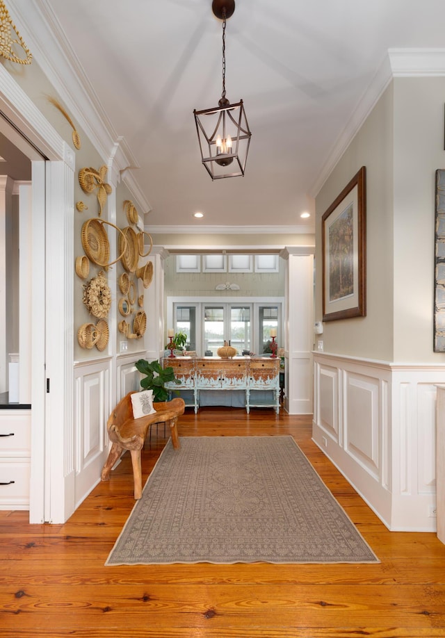 corridor with crown molding, a decorative wall, a chandelier, wood finished floors, and recessed lighting