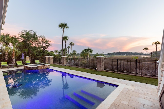 pool at dusk featuring fence, a pool with connected hot tub, and a patio area