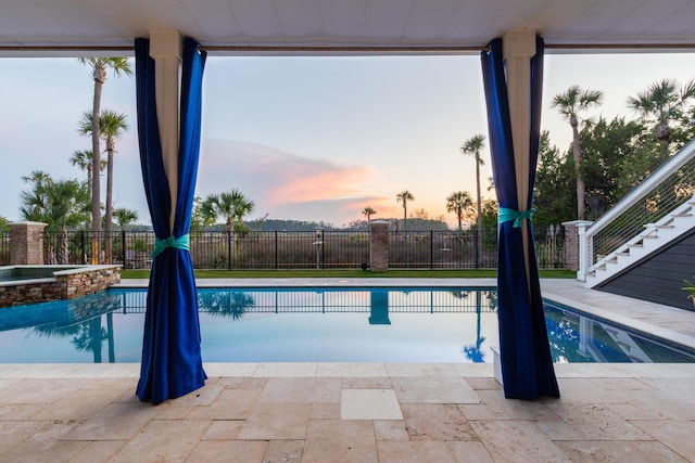 pool at dusk with fence, stairs, and a pool with connected hot tub