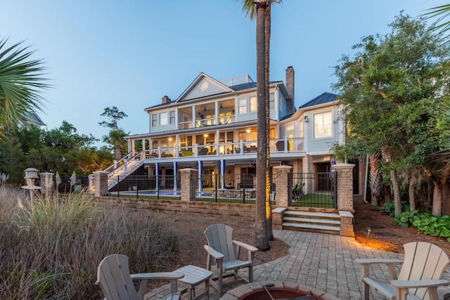 back of property featuring a balcony, a chimney, a patio area, stairway, and fence