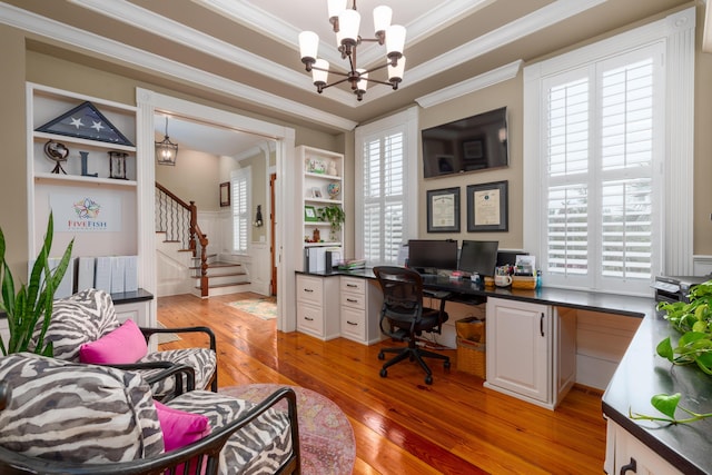office space with a chandelier, crown molding, light wood finished floors, built in desk, and a wainscoted wall