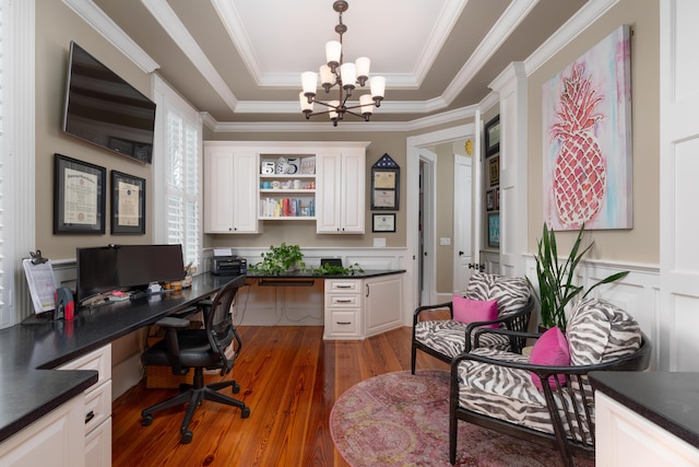 office space with a chandelier, built in desk, a tray ceiling, wood finished floors, and ornamental molding