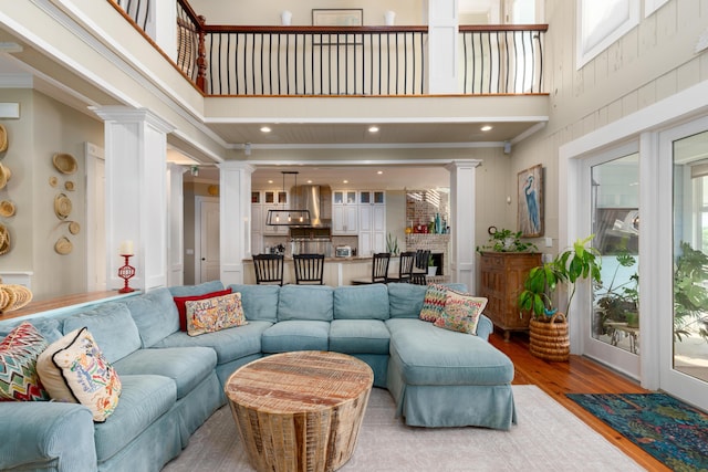 living room featuring ornate columns, a towering ceiling, wood finished floors, recessed lighting, and ornamental molding