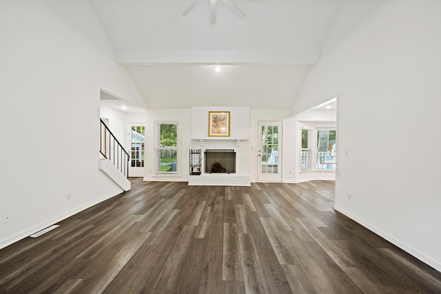 unfurnished living room with a healthy amount of sunlight, dark hardwood / wood-style flooring, beam ceiling, and a brick fireplace