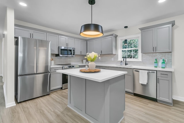 kitchen featuring gray cabinetry, sink, hanging light fixtures, appliances with stainless steel finishes, and light hardwood / wood-style floors