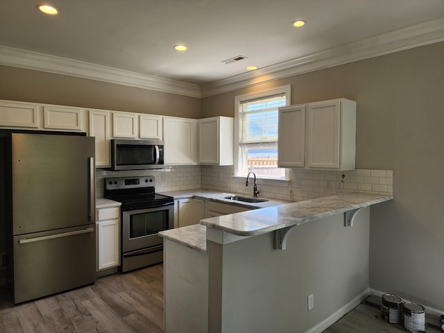 kitchen with white cabinetry, a peninsula, appliances with stainless steel finishes, and a sink