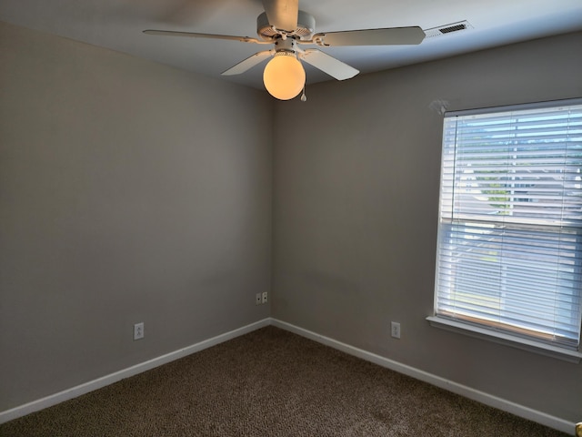 spare room featuring visible vents, a ceiling fan, dark colored carpet, and plenty of natural light