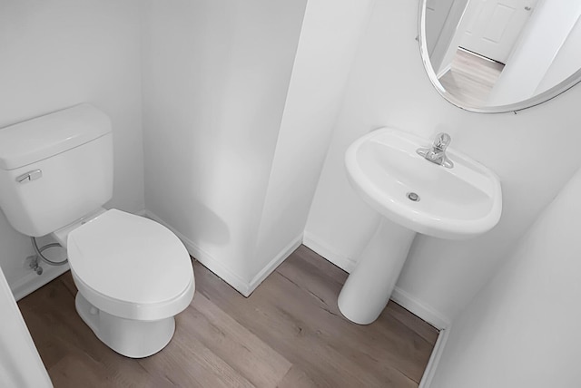 bathroom featuring baseboards, wood finished floors, toilet, and a sink