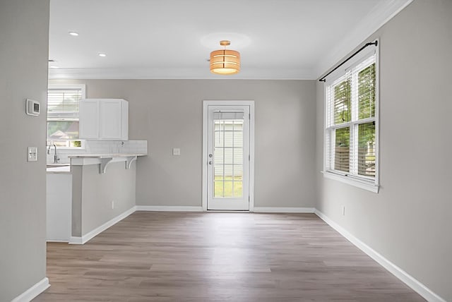 unfurnished dining area featuring a healthy amount of sunlight, crown molding, light wood-style flooring, and baseboards