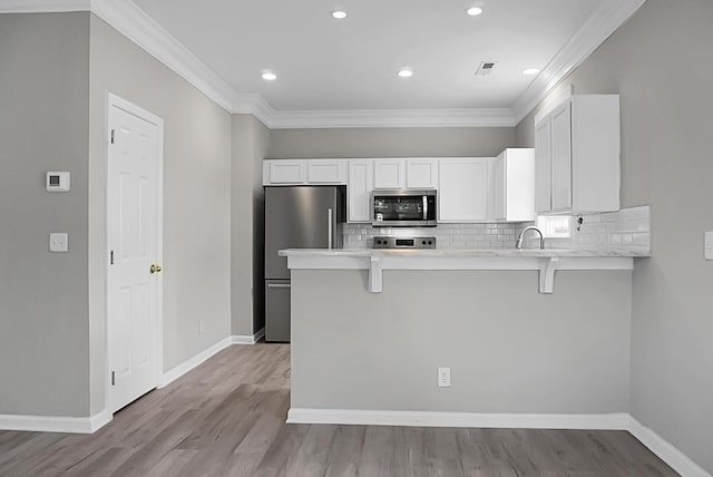 kitchen featuring a breakfast bar area, white cabinets, stainless steel appliances, light countertops, and a peninsula