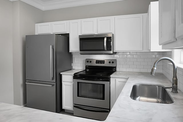 kitchen featuring crown molding, white cabinets, a sink, appliances with stainless steel finishes, and backsplash