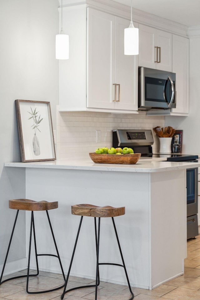 kitchen featuring appliances with stainless steel finishes, white cabinets, backsplash, and a kitchen bar