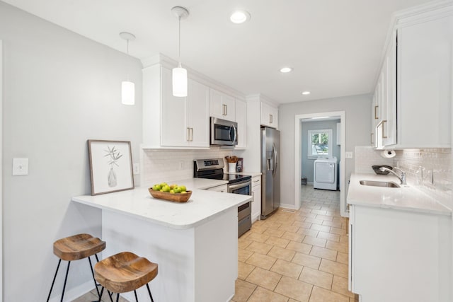 kitchen featuring a breakfast bar, stainless steel appliances, washer / clothes dryer, a sink, and a peninsula