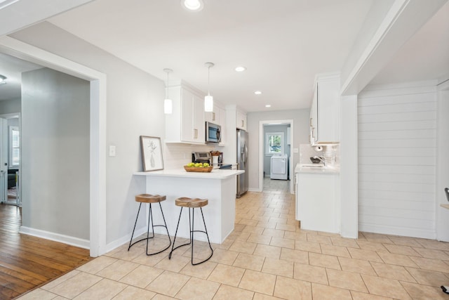 kitchen with stainless steel appliances, light countertops, white cabinets, a sink, and washer / dryer