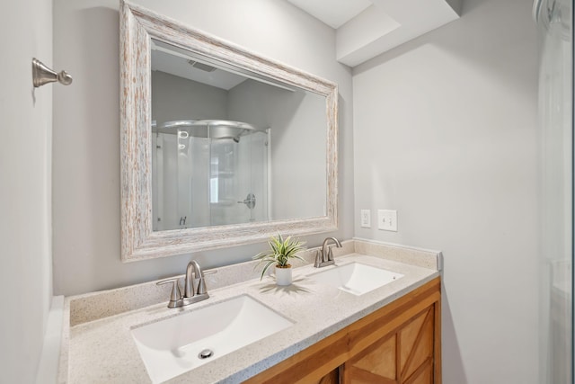 bathroom featuring a shower with shower door, a sink, visible vents, and double vanity