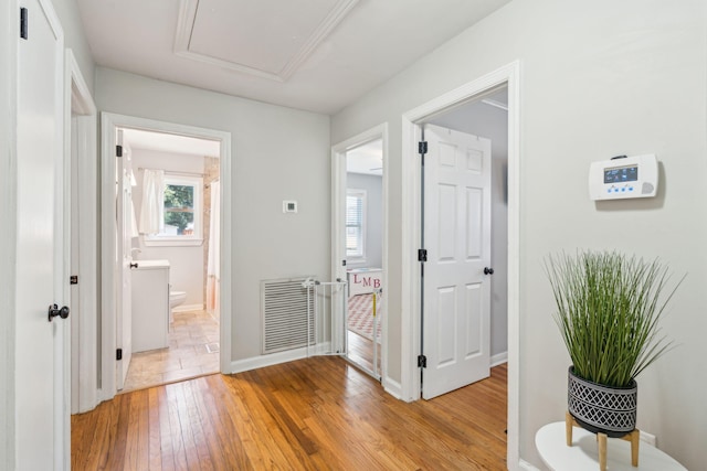 hall with light wood-style floors, baseboards, visible vents, and attic access