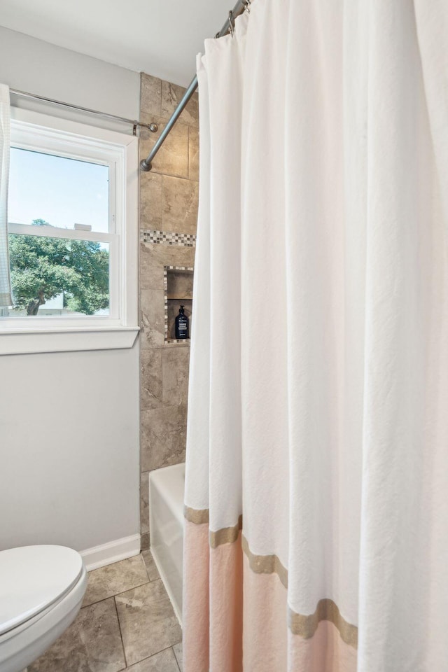 bathroom with toilet, shower / tub combo, and baseboards