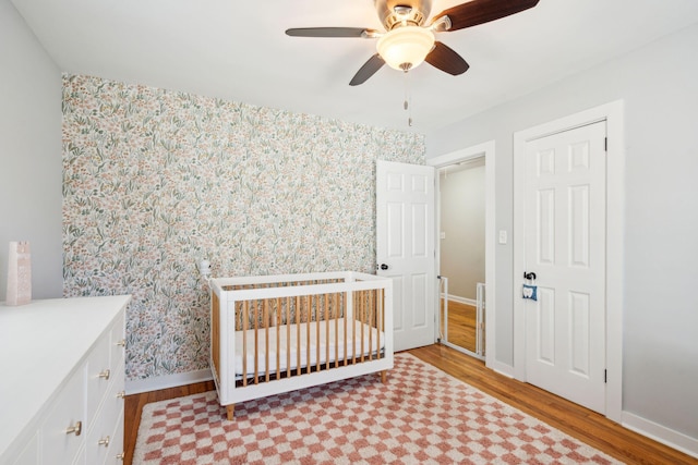 bedroom with a crib, wallpapered walls, baseboards, and wood finished floors