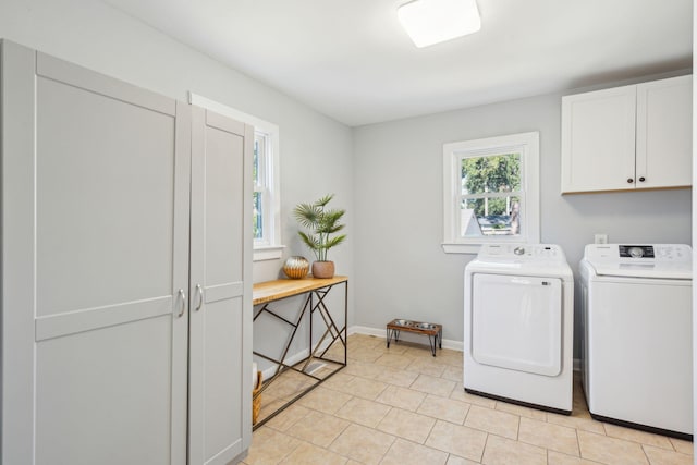 clothes washing area featuring light tile patterned floors, washing machine and dryer, cabinet space, and baseboards