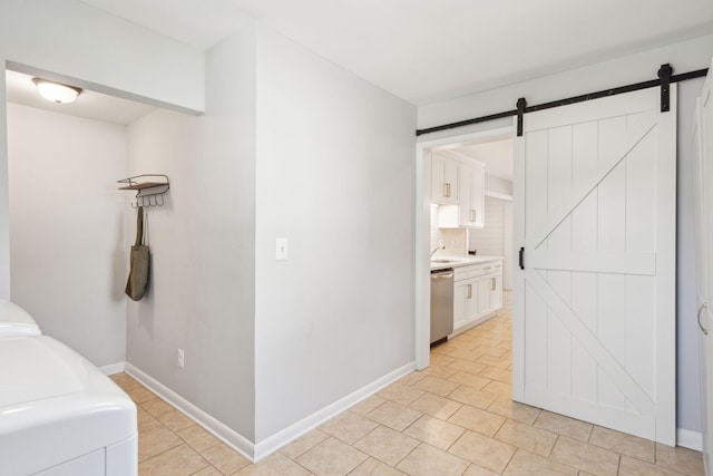 hallway featuring light tile patterned floors, a barn door, washing machine and dryer, a sink, and baseboards