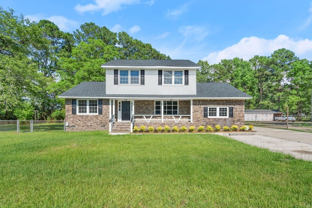 traditional-style home with brick siding, covered porch, a front yard, and fence