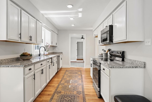 kitchen with light wood-style flooring, ceiling fan, a sink, white cabinets, and appliances with stainless steel finishes