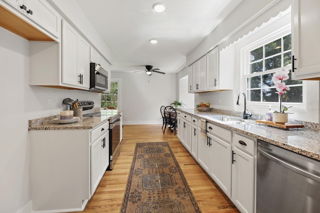 kitchen with a sink, ceiling fan, stainless steel appliances, white cabinets, and light wood-style floors