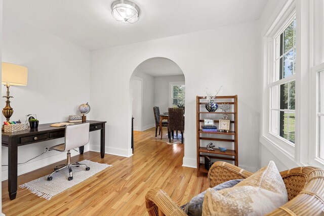 office area with light wood-style flooring, arched walkways, and a wealth of natural light