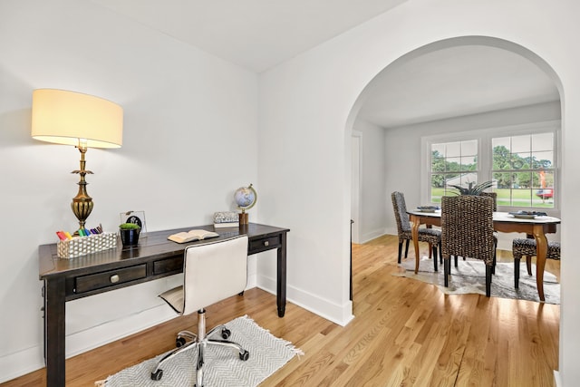 office area with baseboards, arched walkways, and light wood finished floors