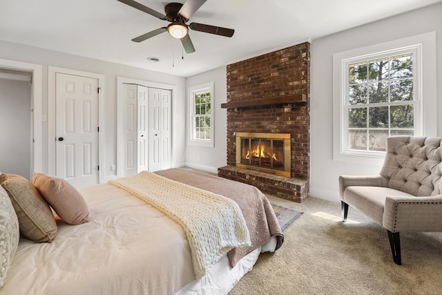 bedroom featuring carpet, visible vents, a ceiling fan, a fireplace, and multiple closets