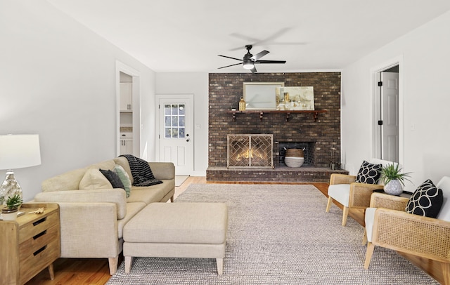 living room featuring a brick fireplace, ceiling fan, and wood finished floors