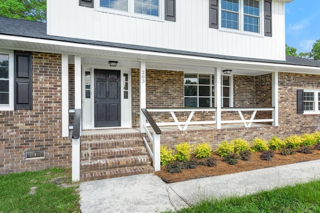 doorway to property featuring crawl space, board and batten siding, brick siding, and covered porch