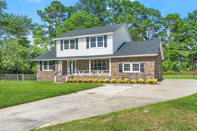 traditional-style house featuring brick siding, covered porch, a front yard, and fence