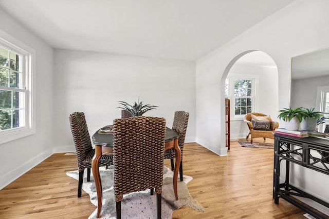 dining space with arched walkways, baseboards, and light wood-style floors