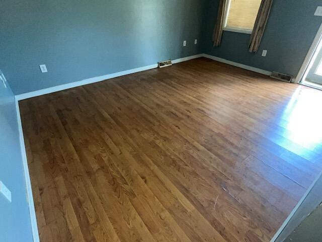 unfurnished room featuring baseboards, visible vents, and dark wood-style floors