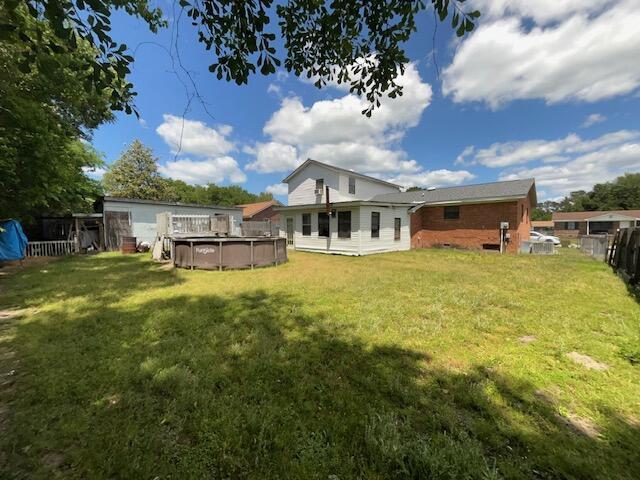 back of house featuring an outdoor pool, fence, and a yard