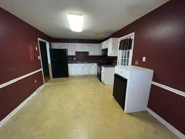 kitchen featuring white cabinets, baseboards, a sink, and black appliances